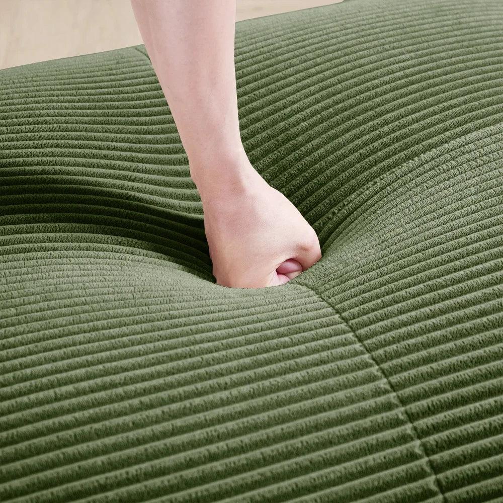 Hand pressing down on green corduroy cushion, showcasing softness at Peak Store
